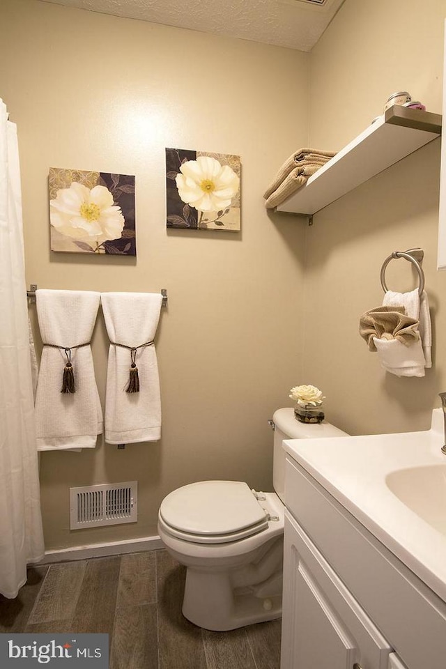 full bath featuring toilet, vanity, wood finished floors, and visible vents