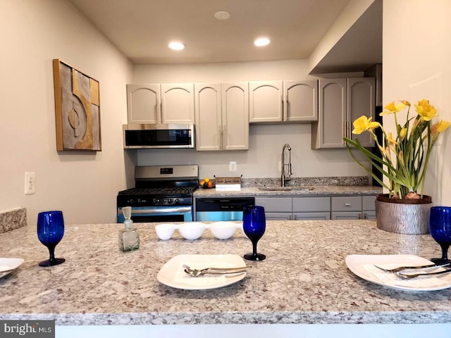 kitchen featuring light stone counters, gray cabinetry, recessed lighting, stainless steel appliances, and a sink