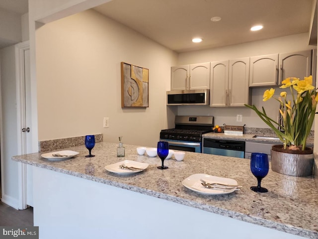 kitchen with recessed lighting, stainless steel appliances, a peninsula, white cabinets, and light stone countertops