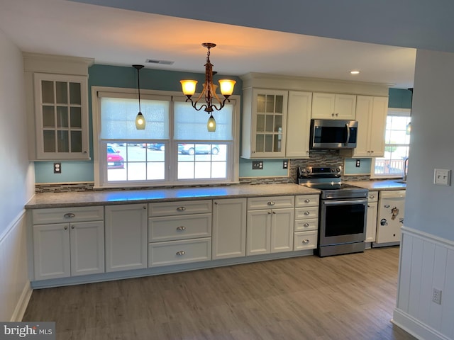 kitchen with stainless steel appliances, visible vents, hanging light fixtures, light wood-type flooring, and wainscoting