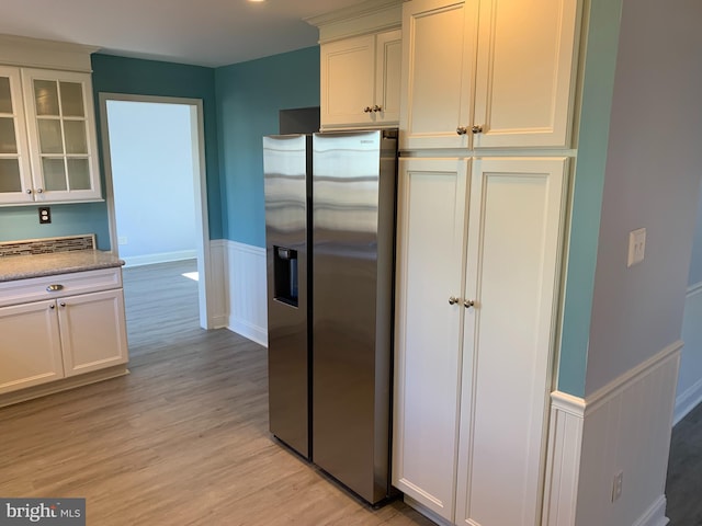 kitchen with a wainscoted wall, light wood-style floors, glass insert cabinets, white cabinetry, and stainless steel fridge with ice dispenser