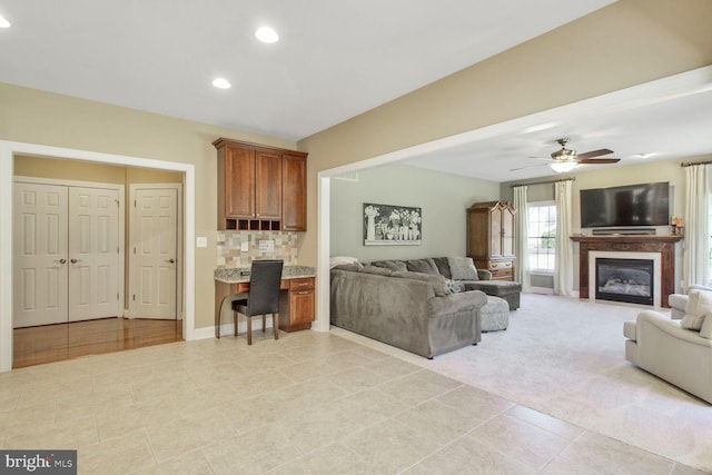 living area featuring baseboards, recessed lighting, ceiling fan, a glass covered fireplace, and light colored carpet