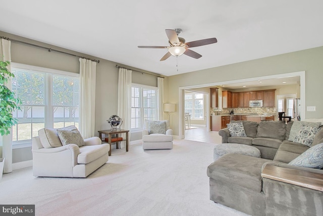 living room featuring light carpet, baseboards, and a ceiling fan