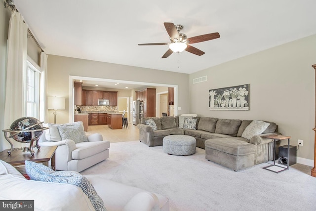 living room with visible vents, light carpet, a ceiling fan, light tile patterned flooring, and baseboards