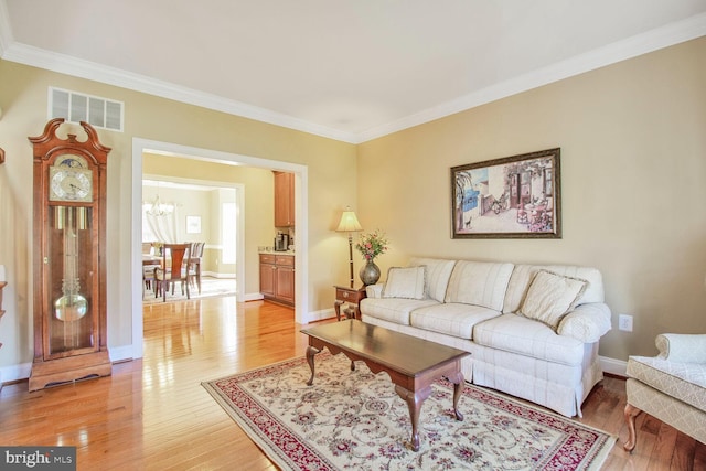 living room featuring baseboards, visible vents, an inviting chandelier, light wood-style flooring, and ornamental molding