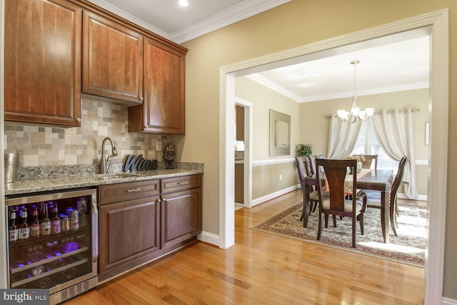 kitchen with beverage cooler, light wood finished floors, a sink, decorative backsplash, and a chandelier