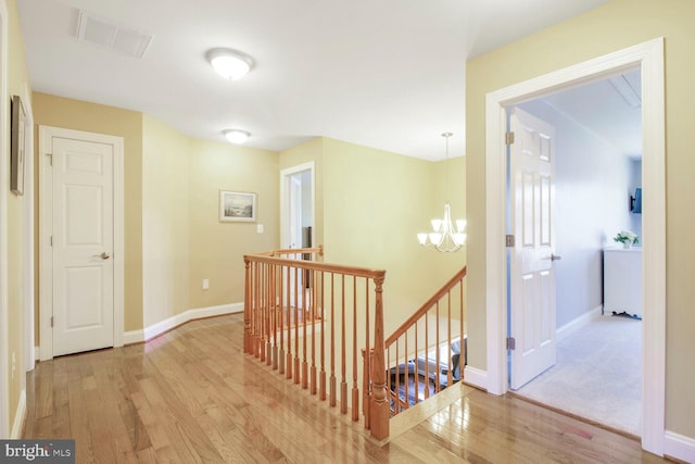 hallway with visible vents, an upstairs landing, a notable chandelier, wood finished floors, and baseboards