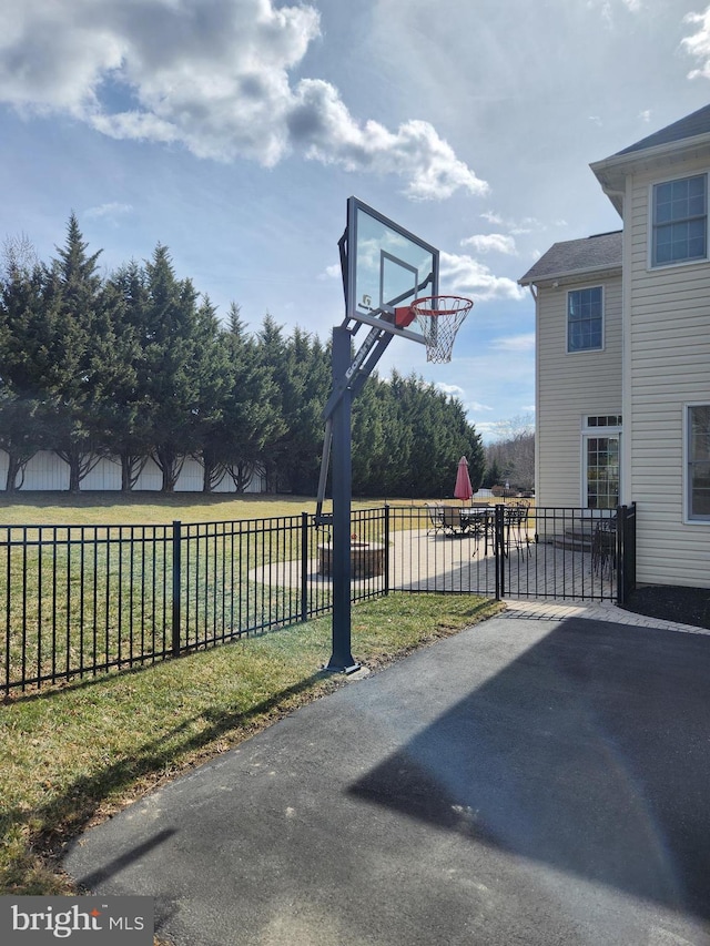 view of basketball court featuring basketball hoop, a yard, and fence