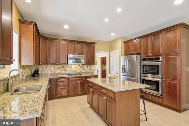 kitchen featuring a sink, light stone counters, tasteful backsplash, a center island, and appliances with stainless steel finishes