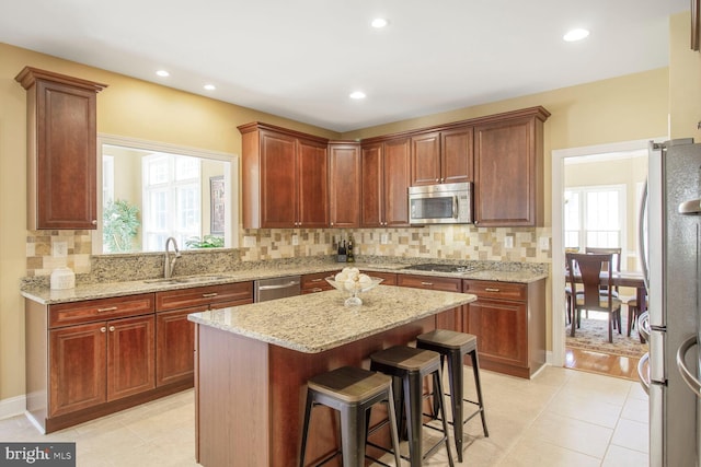 kitchen featuring backsplash, a center island, light stone countertops, appliances with stainless steel finishes, and a sink