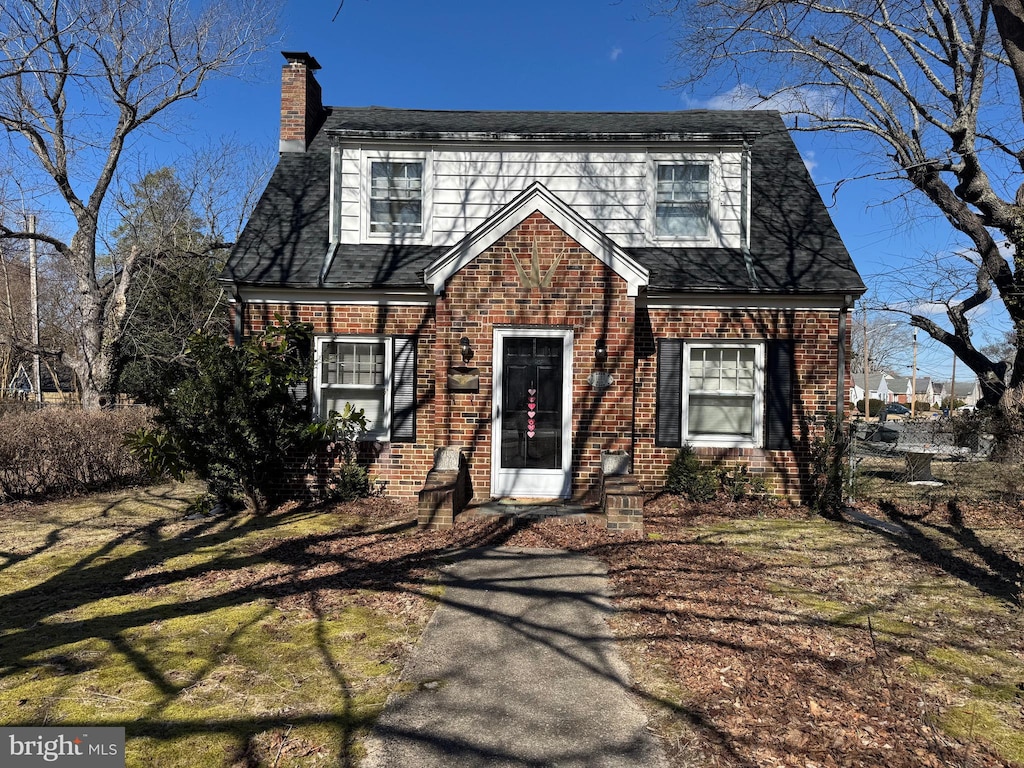 view of front facade with a front yard, roof with shingles, a chimney, and brick siding