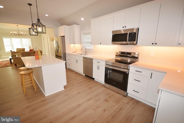 kitchen featuring light wood finished floors, appliances with stainless steel finishes, white cabinets, a sink, and a kitchen island