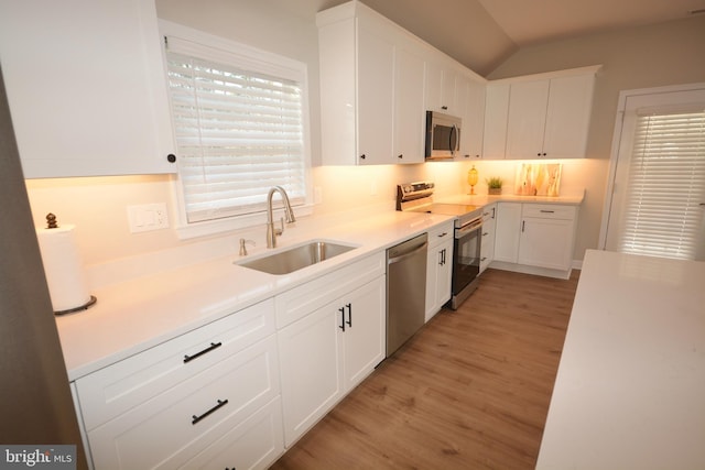 kitchen with light wood finished floors, appliances with stainless steel finishes, a sink, and white cabinetry