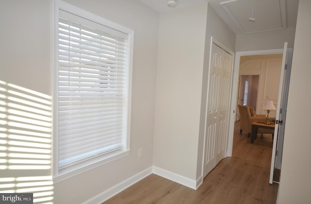 corridor with light wood-style floors, attic access, and baseboards