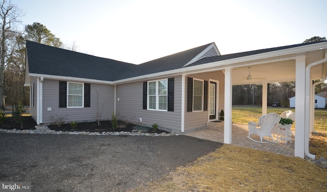 view of side of property with a patio area, aphalt driveway, and roof with shingles