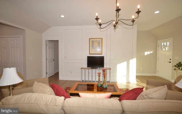 living room featuring lofted ceiling, a notable chandelier, wood finished floors, and a decorative wall