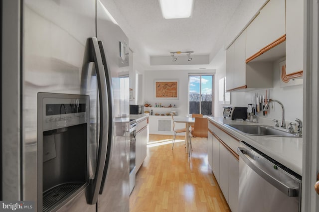 kitchen with light wood finished floors, a raised ceiling, stainless steel appliances, a textured ceiling, and a sink