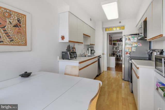 kitchen with stainless steel appliances, light wood-type flooring, light countertops, and a sink