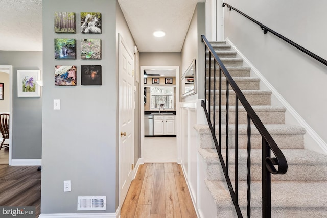 stairway with visible vents, a textured ceiling, baseboards, and wood finished floors