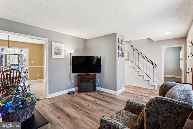 living room with a textured ceiling, stairway, wood finished floors, and baseboards