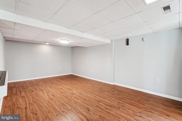 finished below grade area featuring a paneled ceiling, visible vents, baseboards, and wood finished floors