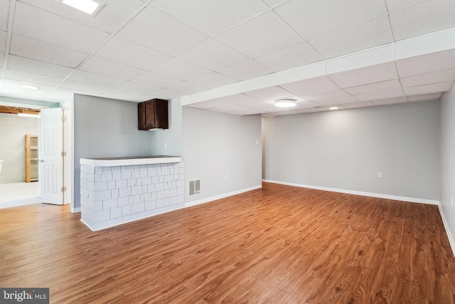 finished below grade area featuring light wood-style flooring, a drop ceiling, visible vents, and baseboards