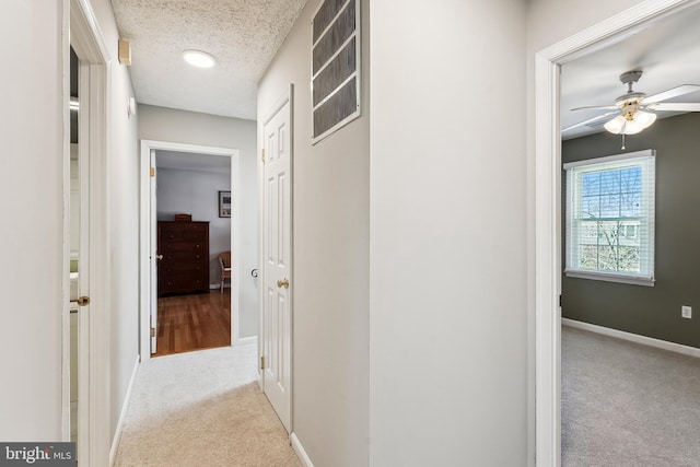 corridor with visible vents, a textured ceiling, baseboards, and carpet flooring