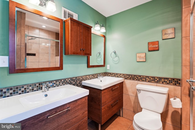 bathroom with tile patterned flooring, toilet, visible vents, tile walls, and a tile shower