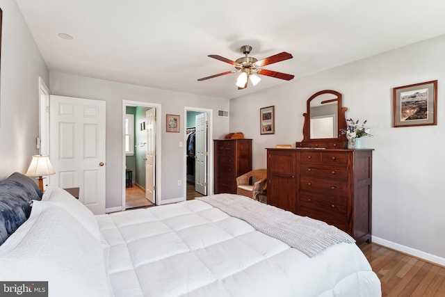 bedroom with ensuite bathroom, ceiling fan, wood finished floors, baseboards, and a walk in closet