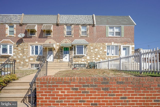 multi unit property featuring stone siding, fence, and brick siding