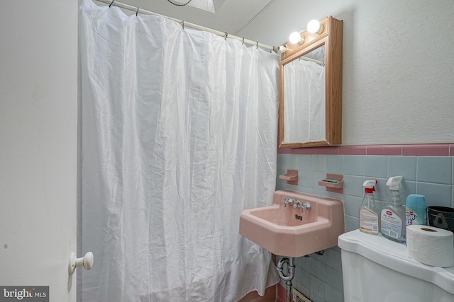 full bath featuring a textured wall, curtained shower, toilet, a sink, and tile walls