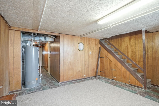 finished basement with water heater, wood walls, and stairway