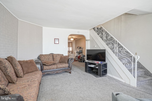 living room featuring arched walkways, brick wall, stairway, and carpet flooring