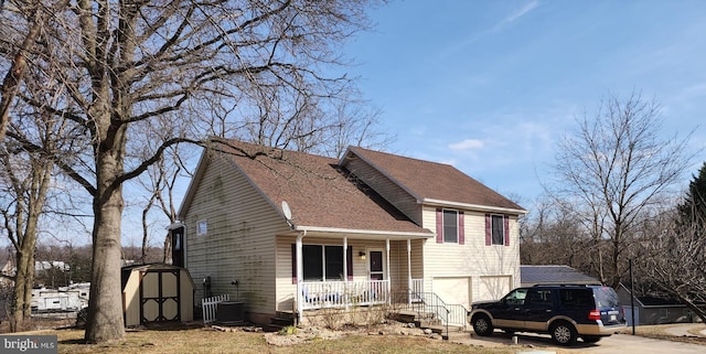 view of front of property with central air condition unit, a porch, concrete driveway, an attached garage, and a storage shed