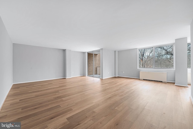 unfurnished living room featuring radiator, baseboards, and light wood finished floors