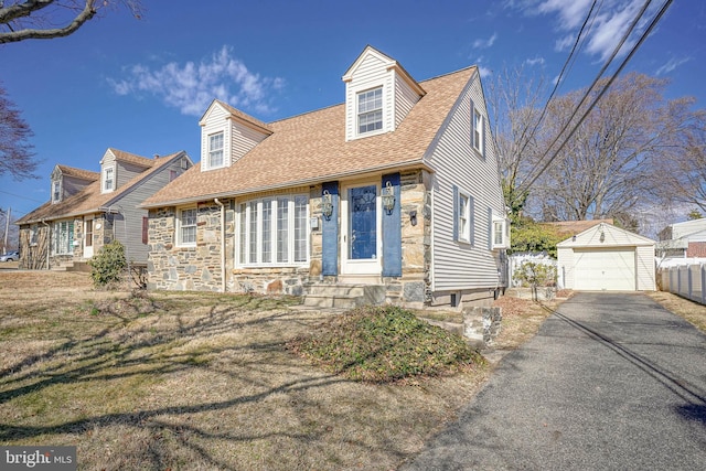 cape cod house featuring an outbuilding, a shingled roof, a garage, stone siding, and driveway