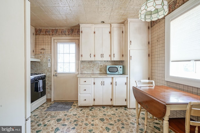 kitchen with under cabinet range hood, white cabinets, light countertops, gas stove, and wallpapered walls