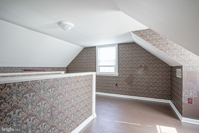 additional living space featuring lofted ceiling, wallpapered walls, baseboards, and wood finished floors