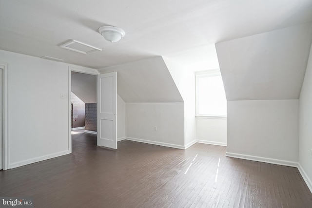 additional living space with attic access, dark wood-type flooring, vaulted ceiling, and baseboards