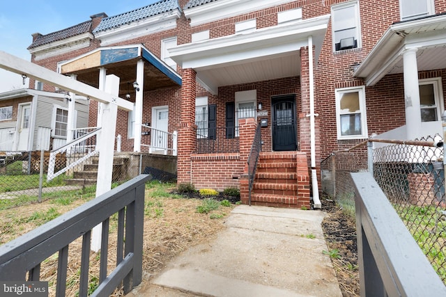 property entrance featuring a tile roof, covered porch, brick siding, and fence