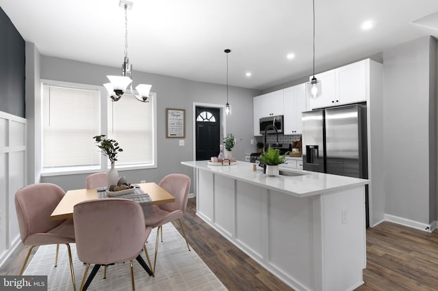 kitchen featuring a kitchen island with sink, dark wood-type flooring, light countertops, appliances with stainless steel finishes, and backsplash