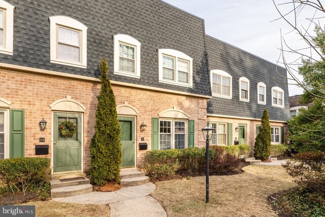 view of property with entry steps, brick siding, mansard roof, and roof with shingles