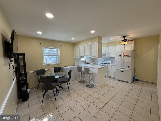 kitchen with white appliances, a peninsula, a sink, white cabinetry, and backsplash