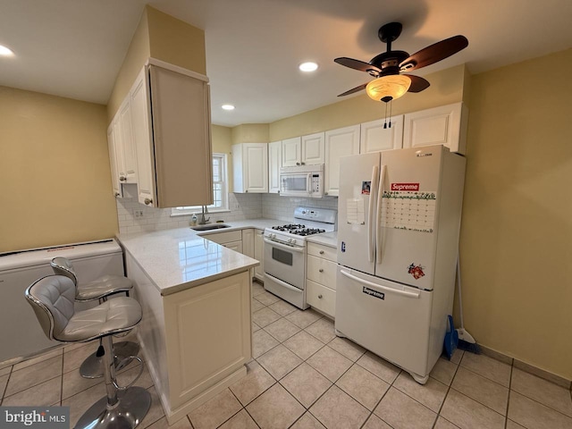 kitchen featuring tasteful backsplash, light countertops, white cabinets, white appliances, and a peninsula