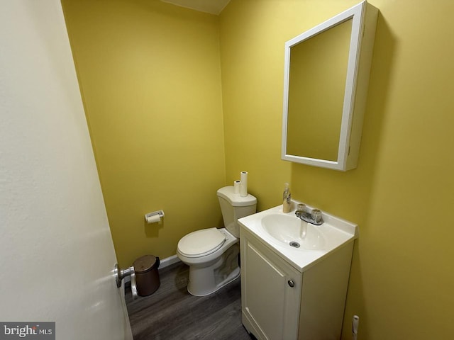 half bathroom featuring toilet, baseboards, wood finished floors, and vanity