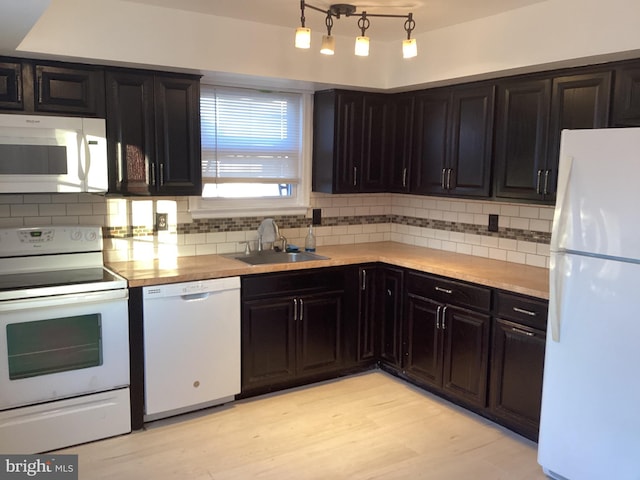 kitchen with light countertops, light wood-style flooring, backsplash, a sink, and white appliances