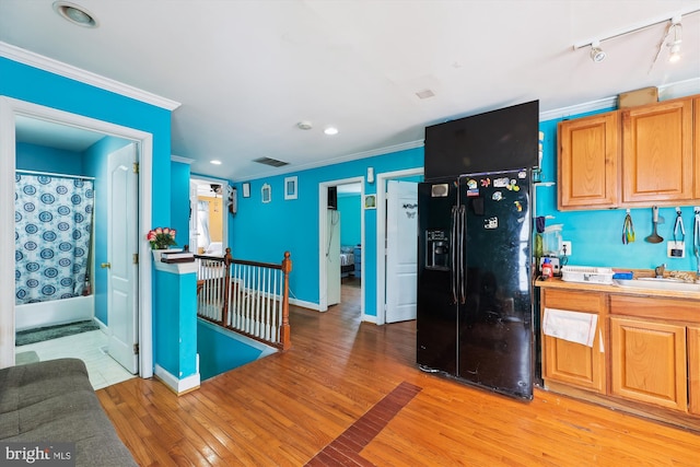 kitchen featuring black refrigerator with ice dispenser, ornamental molding, baseboards, light wood finished floors, and visible vents