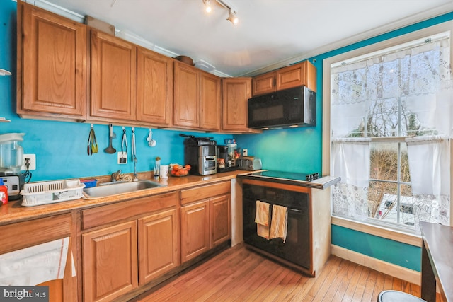 kitchen with a sink, black microwave, brown cabinetry, and light wood finished floors