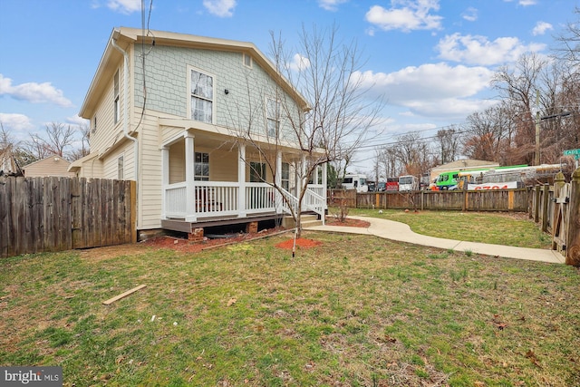 rear view of property featuring a fenced backyard, a lawn, and covered porch