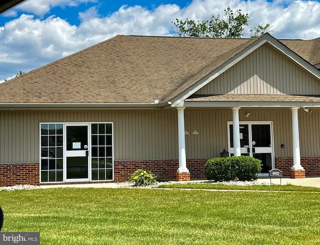 view of front of house featuring a front yard, roof with shingles, and brick siding